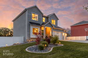 Modern two-story residence featuring a two-car garage, white vinyl fencing, and a manicured lawn with decorative rock landscaping