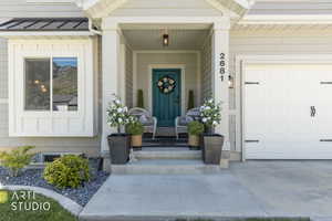 Welcoming entry with a teal door and covered porch, featuring a white paneled garage door, a bay window, and organized landscaping with dark stone