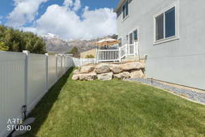 Expansive backyard featuring a manicured lawn, white privacy fencing, and a retaining wall of natural boulders