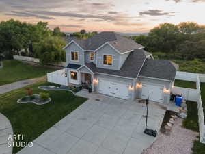 Modern transitional home featuring light gray siding, dark gray roof, a two-car garage, established front landscaping, and a white privacy fence