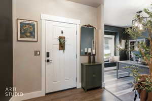 Entryway featuring a paneled white door with smart lock hardware, a dark wood-finish flooring, and a decorative wall mirror