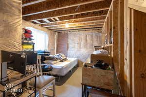 Unfinished basement featuring exposed wood joists, a visible window, and partial brick wall detailing