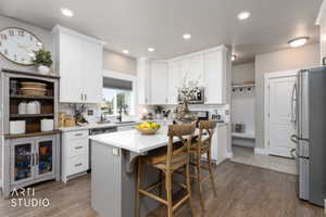 Modern kitchen featuring white cabinetry, a light-toned island with seating, stainless steel appliances, and wood-finish flooring
