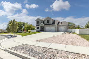 Two-story residence featuring light gray siding with dark trim, a concrete driveway, a three-car garage, manicured lawn, and a white picket fence