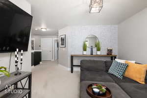 Living area featuring light-colored carpeting, a light gray accent wall with textured wallpaper, and a contemporary ceiling light fixture
