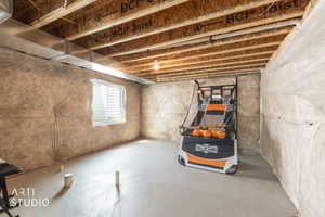 Unfinished basement featuring exposed wood joists, insulated walls, concrete flooring, and a sliding window