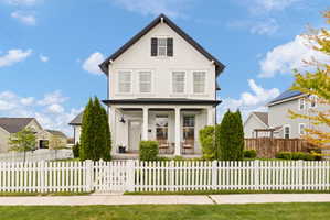 Two-story residence featuring a white picket fence, covered front porch with columns, a prominent gabled roofline, and dormer window with shutters