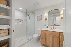White subway tile shower with a glass enclosure, built-in shelving, natural wood-finish vanity, and a white countertop with an undermount sink