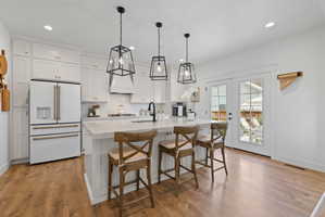 White shaker cabinetry with gold-tone hardware, a tiled backsplash, and light wood-finish flooring