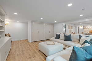 Spacious room featuring wood-finish flooring, recessed lighting, built-in cabinetry with open shelving, and a pair of double-door closets