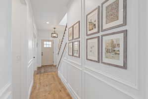Entryway featuring wood-finish flooring, wainscoting, an overhead chandelier, and a staircase with wood handrails