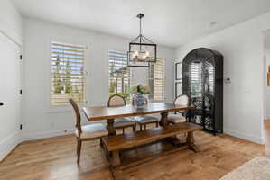 Dining area featuring wood-finish flooring, two large windows with plantation shutters, a contemporary black metal chandelier, and crisp white walls