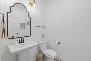 Pedestal sink with a matte black faucet, complemented by a decorative mirror and brass-finish wall sconce