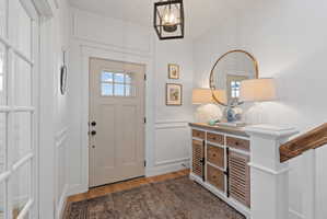 Entryway featuring a paneled door with glass inserts, wood-finish flooring, and white wainscoting