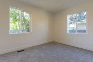 Bright interior space featuring two large windows, neutral wall paint, gray carpeting, white trim, and a floor-level vent