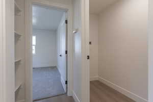 Open doorway leading to a room with light gray carpet and a single window, featuring white walls and baseboards