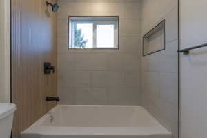 Tub and shower combination featuring large format tile surround, built-in recessed shelf, and matte black fixtures