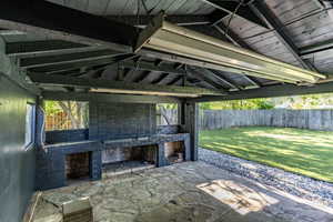 Covered patio featuring a stone slab floor, exposed wood beam ceiling, and a built-in brick structure with two open bays