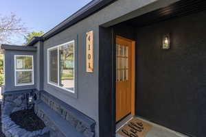 Contemporary exterior featuring dark stucco siding, a vibrant orange front door with glass lites, a wooden address plaque, and a bay window with white framing