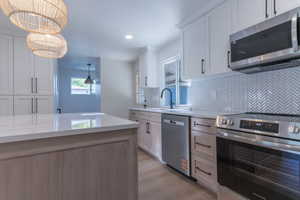 Kitchen featuring a white quartz-finish island, white shaker cabinetry, stainless steel appliances, and a herringbone-patterned tile backsplash