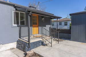 Inviting covered entry featuring a paneled wood-finish door, black metal handrails, and a stone-clad porch foundation