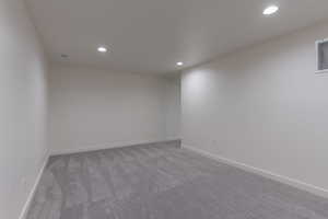 Spacious room featuring light gray patterned carpeting, white baseboards, and recessed lighting fixtures