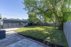 Expansive backyard featuring a manicured lawn, established shade trees, a wooden privacy fence, a detached garage with a window, and a separate shed structure