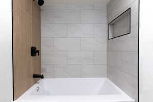 Bathtub featuring matte black fixtures, white subway tile surround, wood-finish accent wall, and a recessed shower niche
