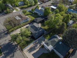 Aerial view showcasing a residential property with a dark shingle roof and light-colored siding, featuring a green lawn, mature trees, and a concrete driveway