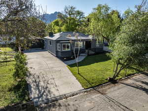 Contemporary gray exterior with dark stone accents, a deep green lawn, a concrete driveway, and a mountain backdrop
