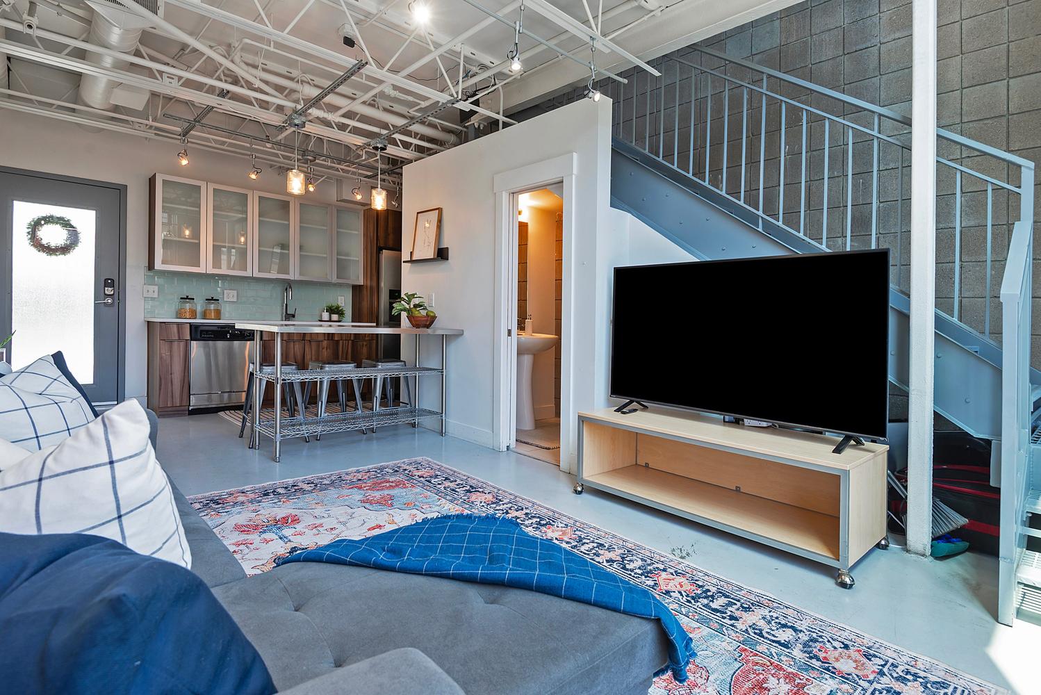 Open-concept living space featuring exposed ceiling ductwork, concrete flooring, and a metal staircase with industrial railing