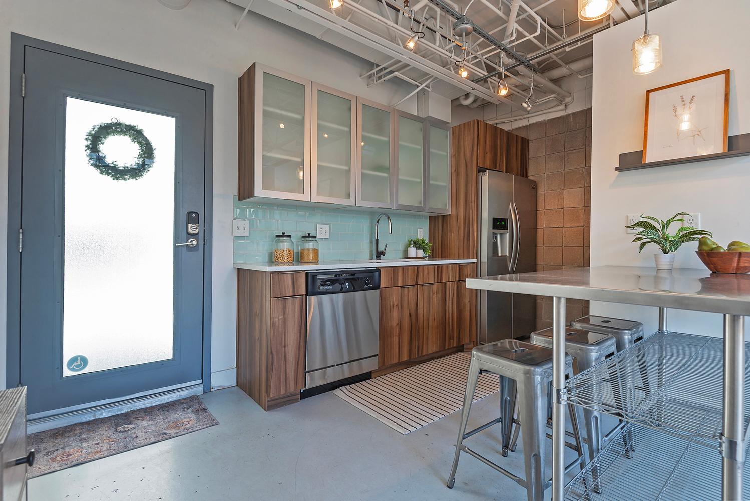 Modern kitchen featuring wood-finish lower cabinetry, stainless steel appliances, and a light blue tile backsplash