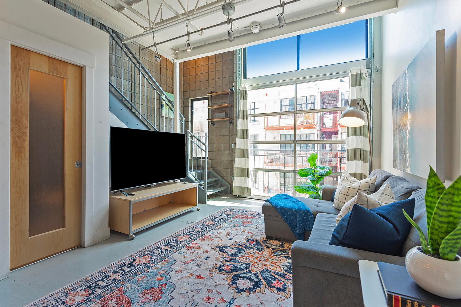 Open-concept living area featuring a full-height glass garage door, exposed ceiling beams with track lighting, and a spiral staircase