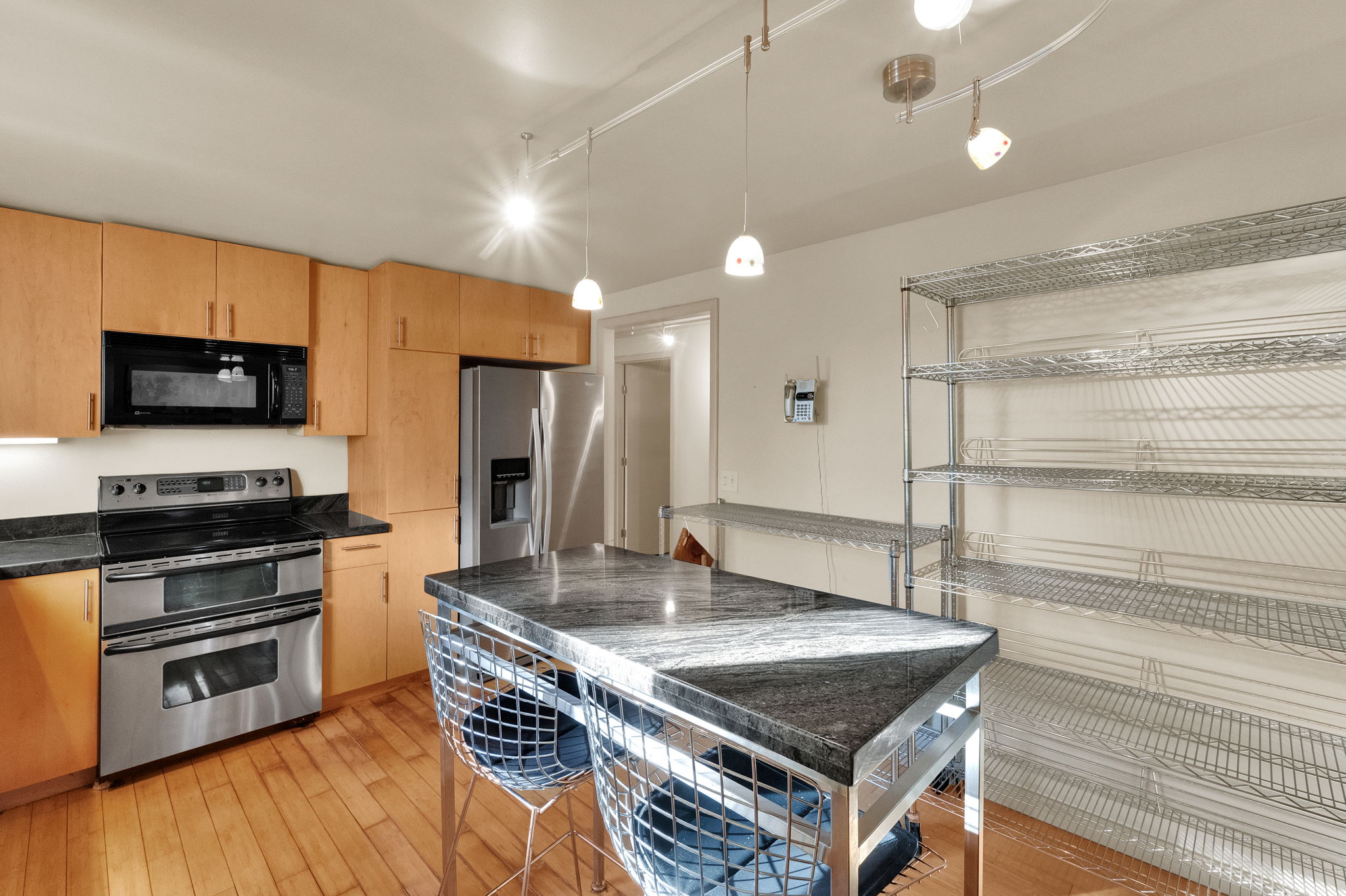 Kitchen featuring light wood cabinetry, stainless steel appliances, dark stone countertops, wood-finish flooring, and a central island with a stone top