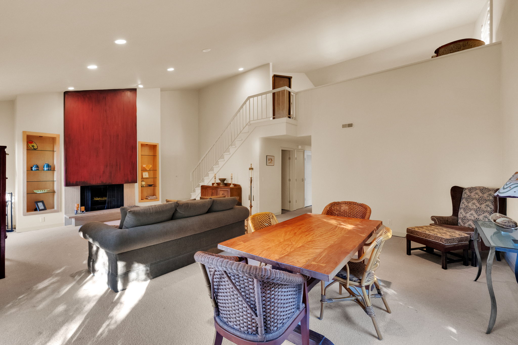Living area featuring a fireplace with a stone hearth, built-in recessed shelving, a vaulted ceiling, recessed lighting, and a staircase with a metal railing
