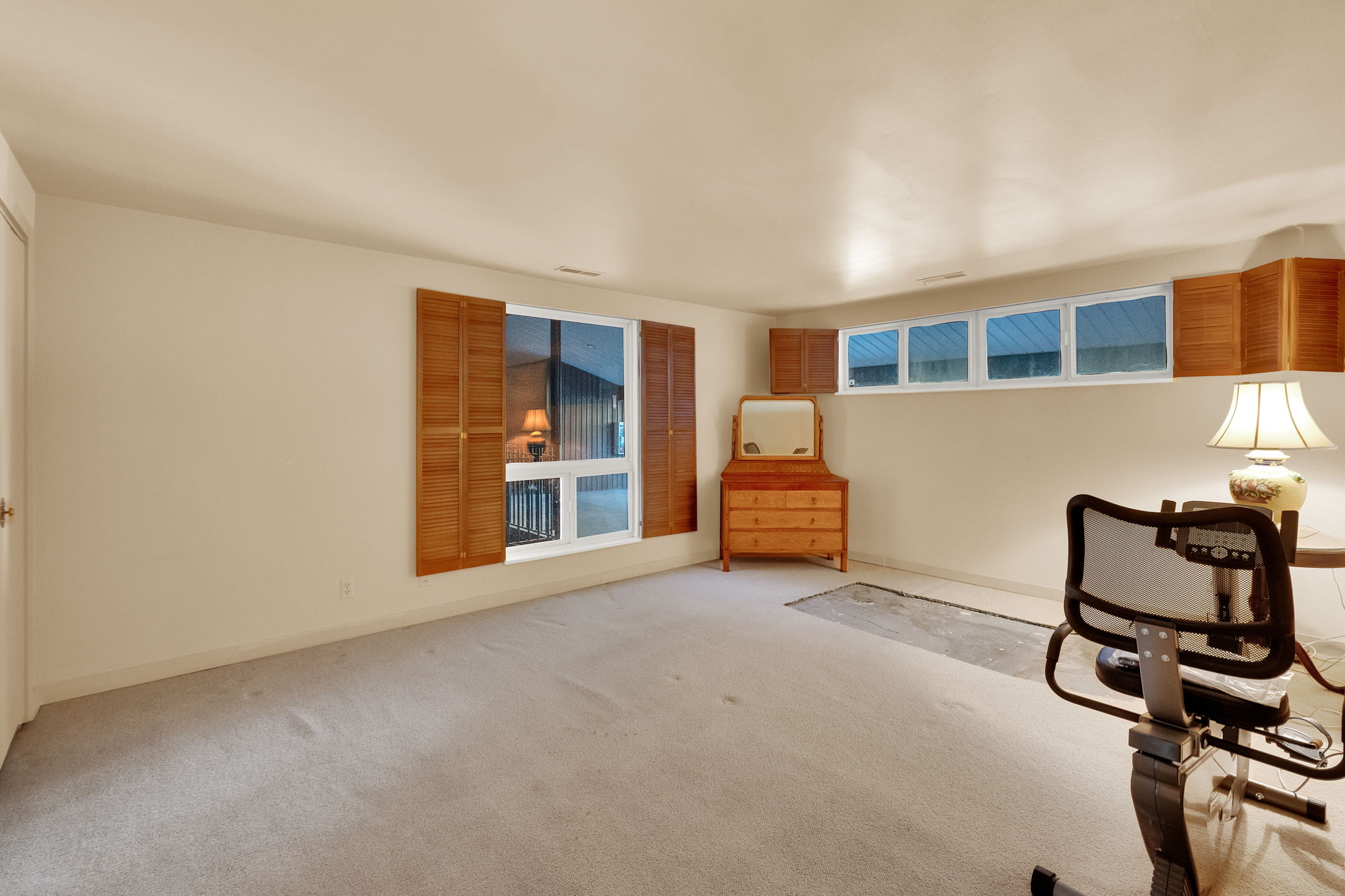 Carpeted room with a large window featuring wood shutters and a row of high transom windows