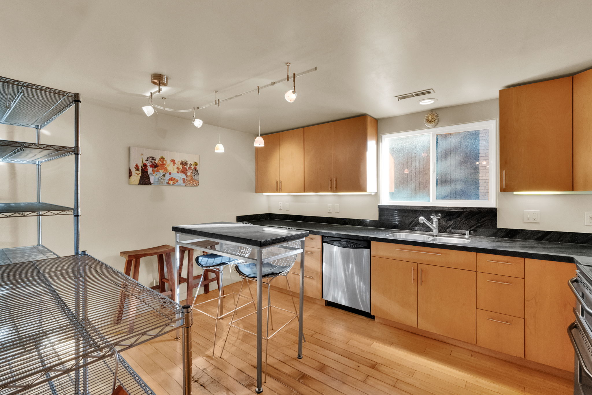 Kitchen featuring wood-finish flooring, ample wood cabinetry, dark countertops, a stainless steel dishwasher, and a double-pane window