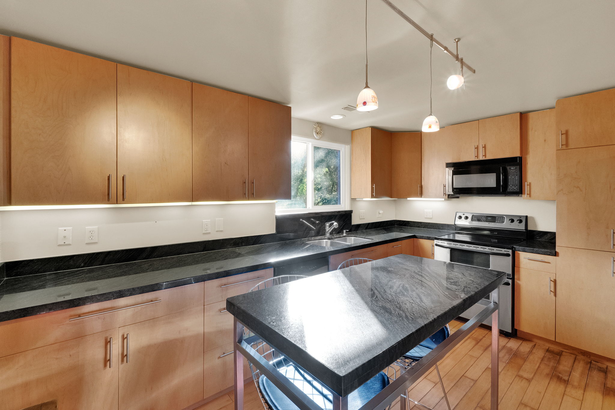Modern kitchen featuring extensive wood cabinetry, dark stone countertops, and wood-finish flooring