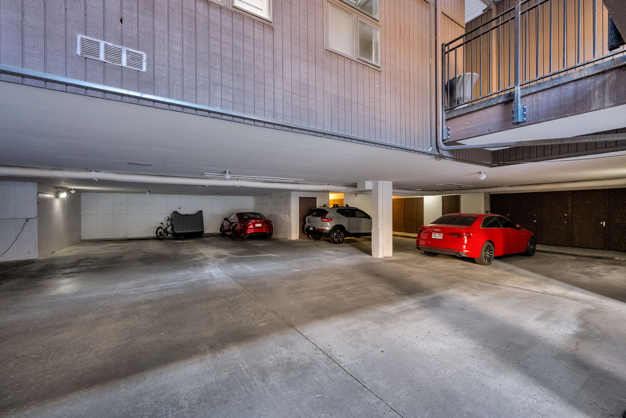 Expansive covered parking area featuring a concrete surface, ample lighting, and individual storage units with dark wood doors