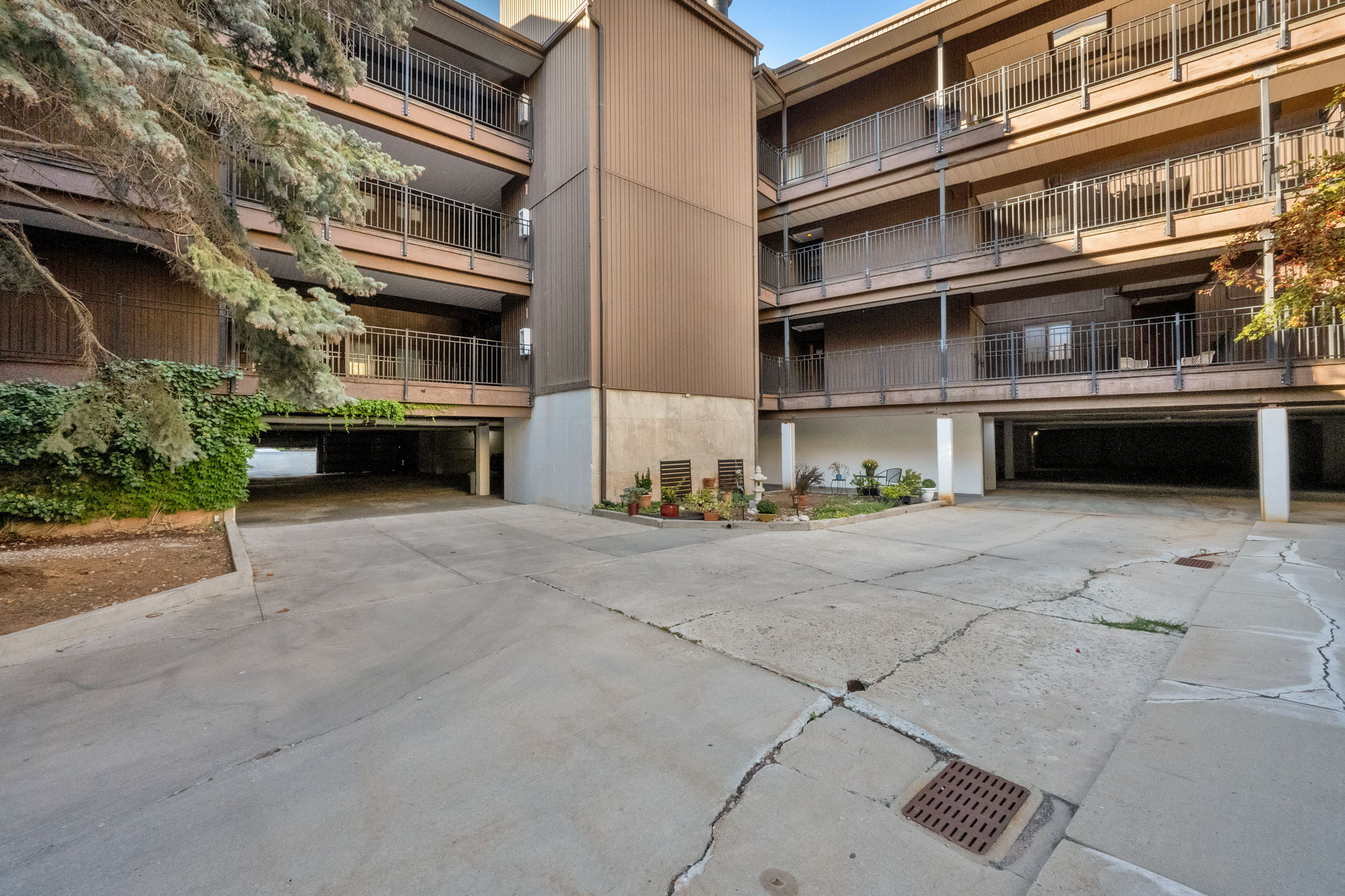 Multi-story building exterior featuring brown siding, multiple balconies with metal railings, and ground-level covered parking