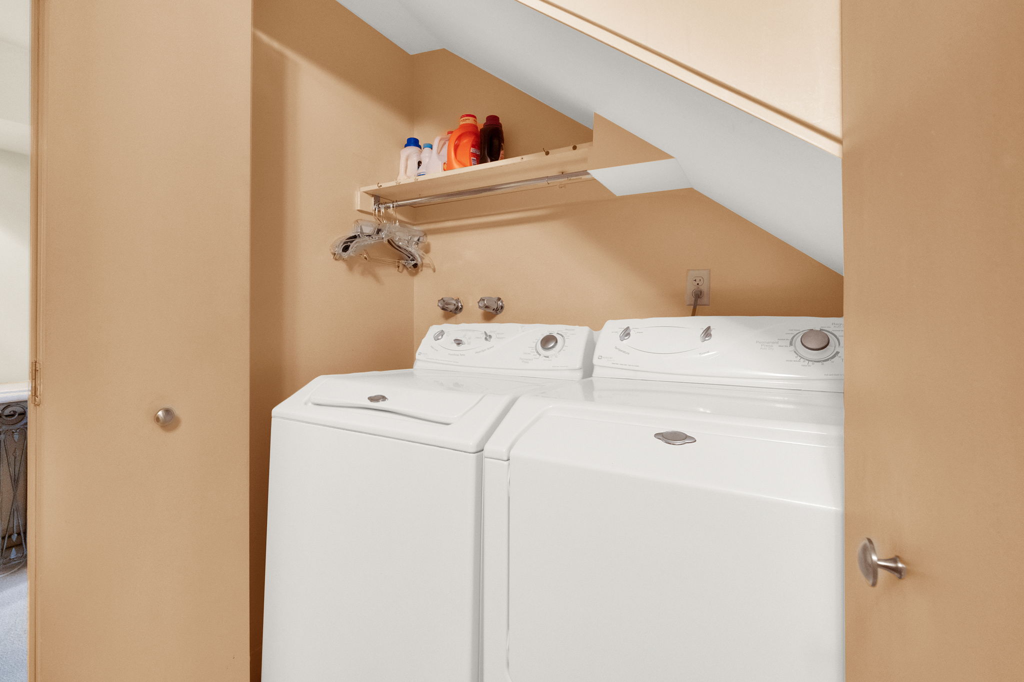 Dedicated laundry area featuring a white washing machine and dryer, a wall-mounted storage shelf, and a built-in hanging rod