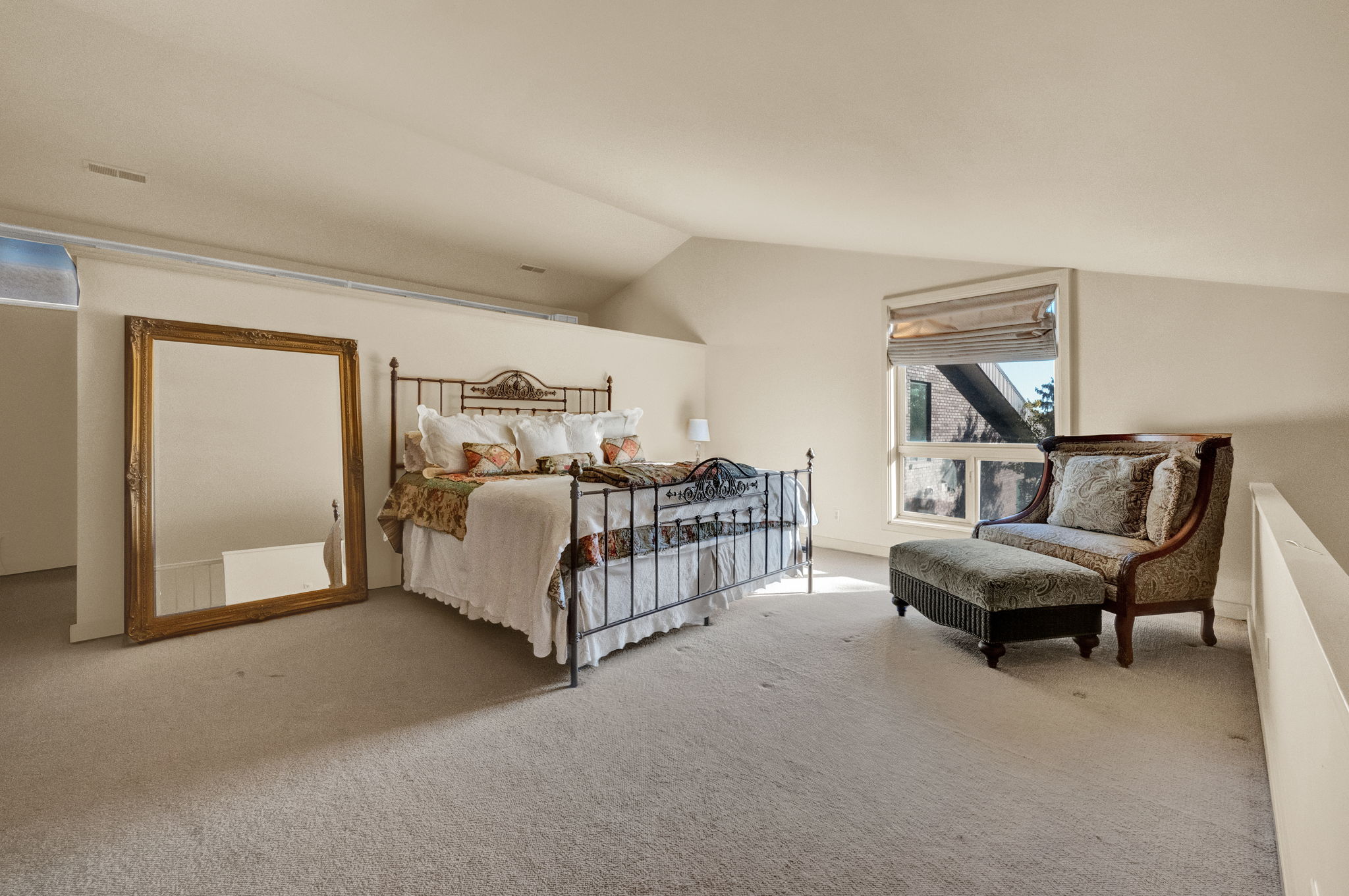 Spacious carpeted room featuring vaulted ceilings, a window with exterior architectural elements visible, and a half-wall partition