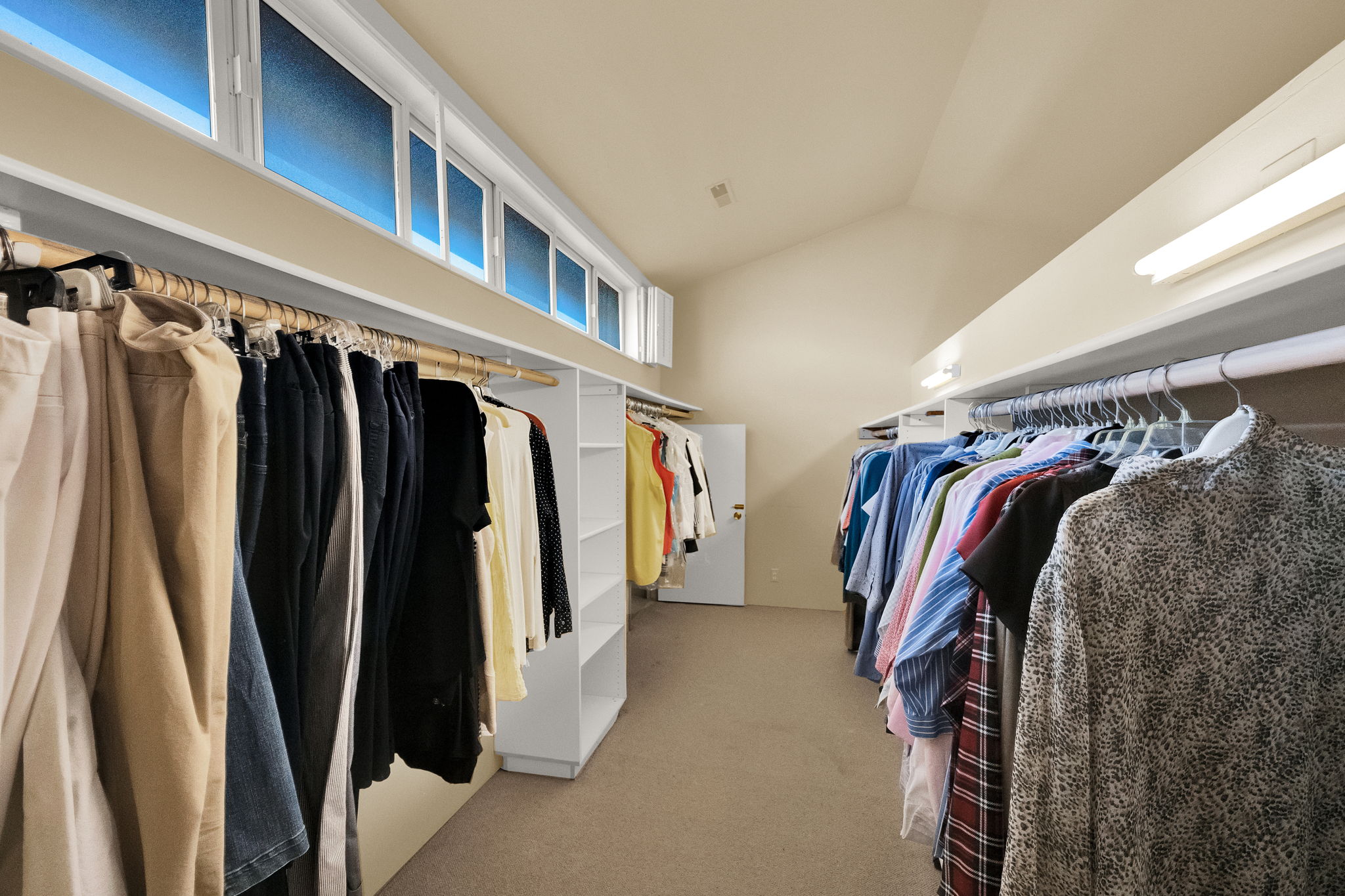 Spacious walk-in closet featuring extensive built-in shelving, multiple clothing rods, and high transom windows