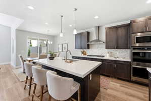 Spacious kitchen featuring a large island quartz countertop, dark wood cabinetry, stainless steel appliances including double ovens and gas cooktop