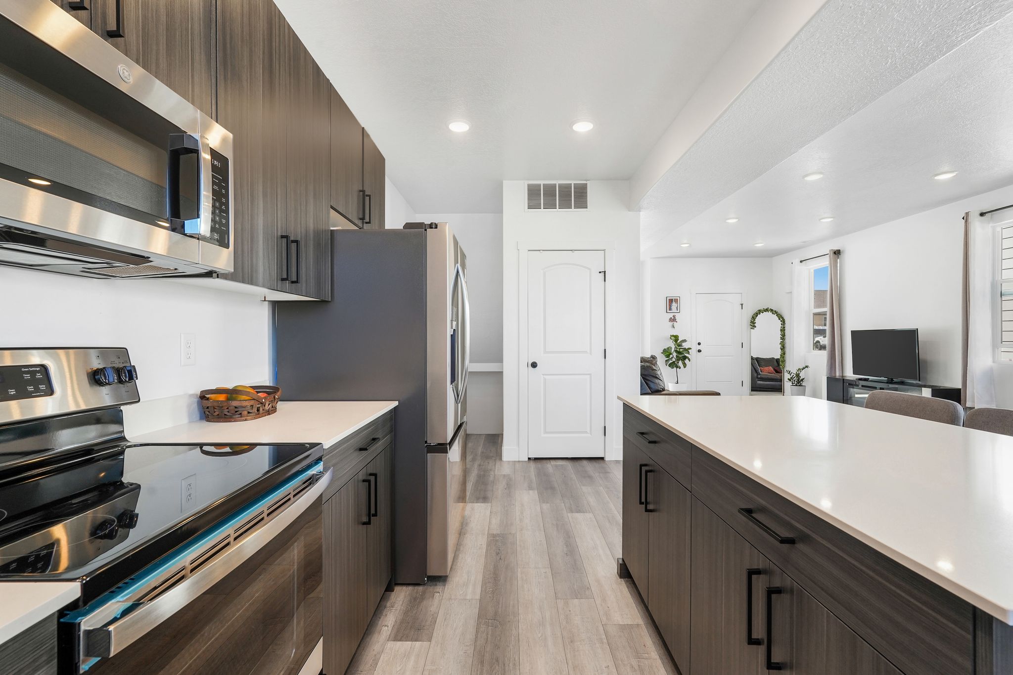Contemporary kitchen featuring sleek dark wood-finish cabinetry, stainless steel appliances, and light-toned countertops