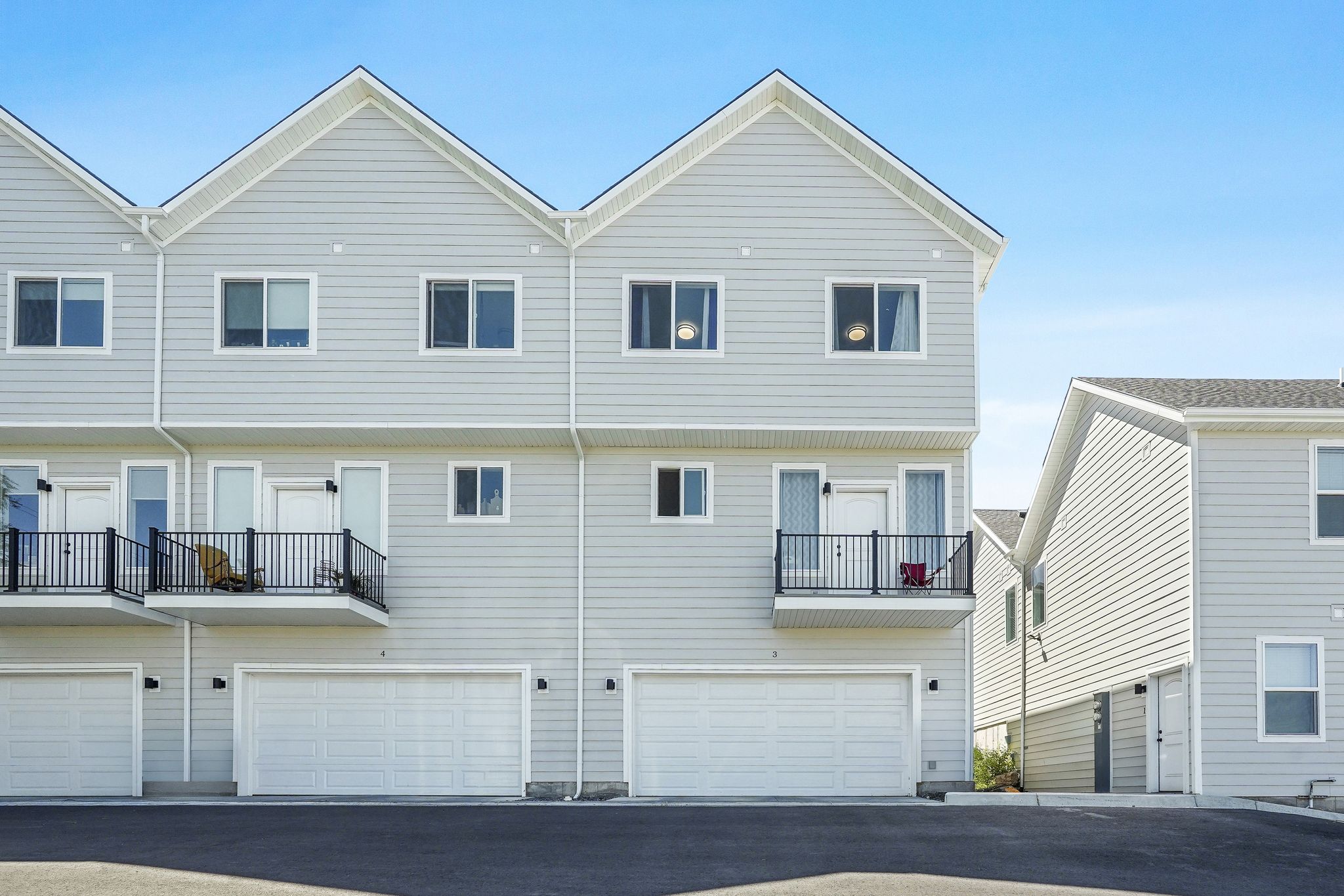 Modern townhome exterior featuring light gray horizontal siding, white trim, and a prominent gable roofline