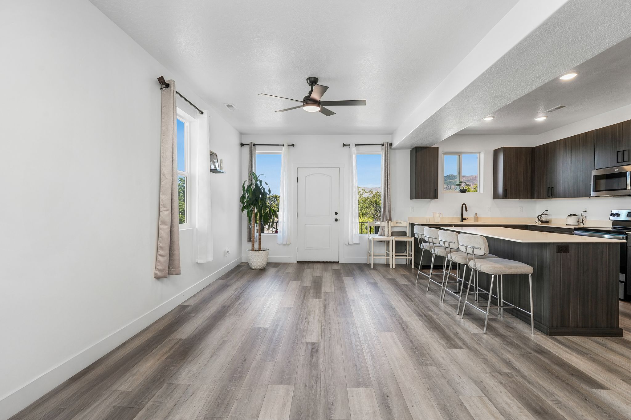 Open-concept living area with wood-finish flooring, white walls, and a ceiling fan