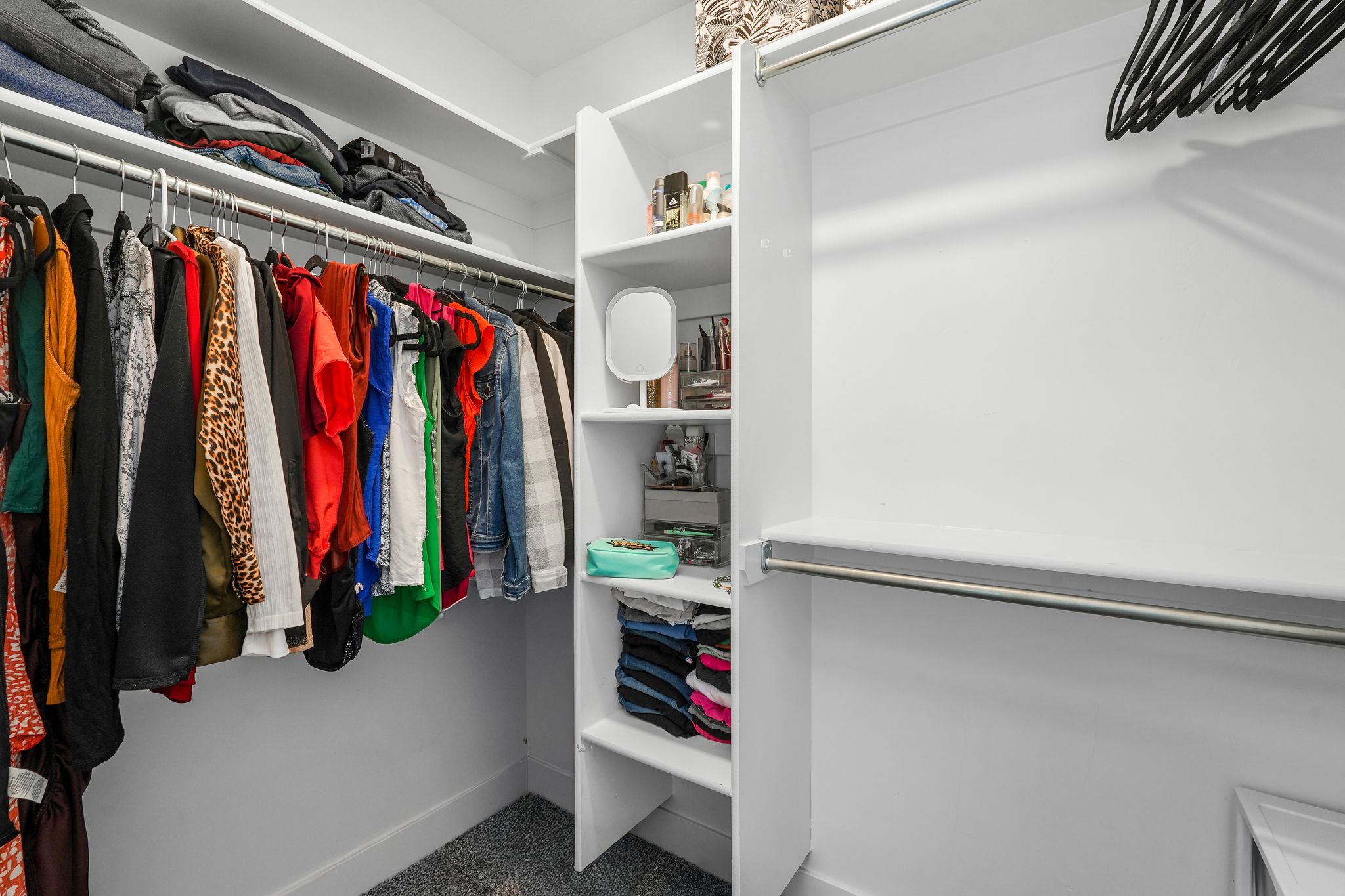 Walk-in closet featuring white built-in shelving, multiple hanging rods, and grey carpet flooring