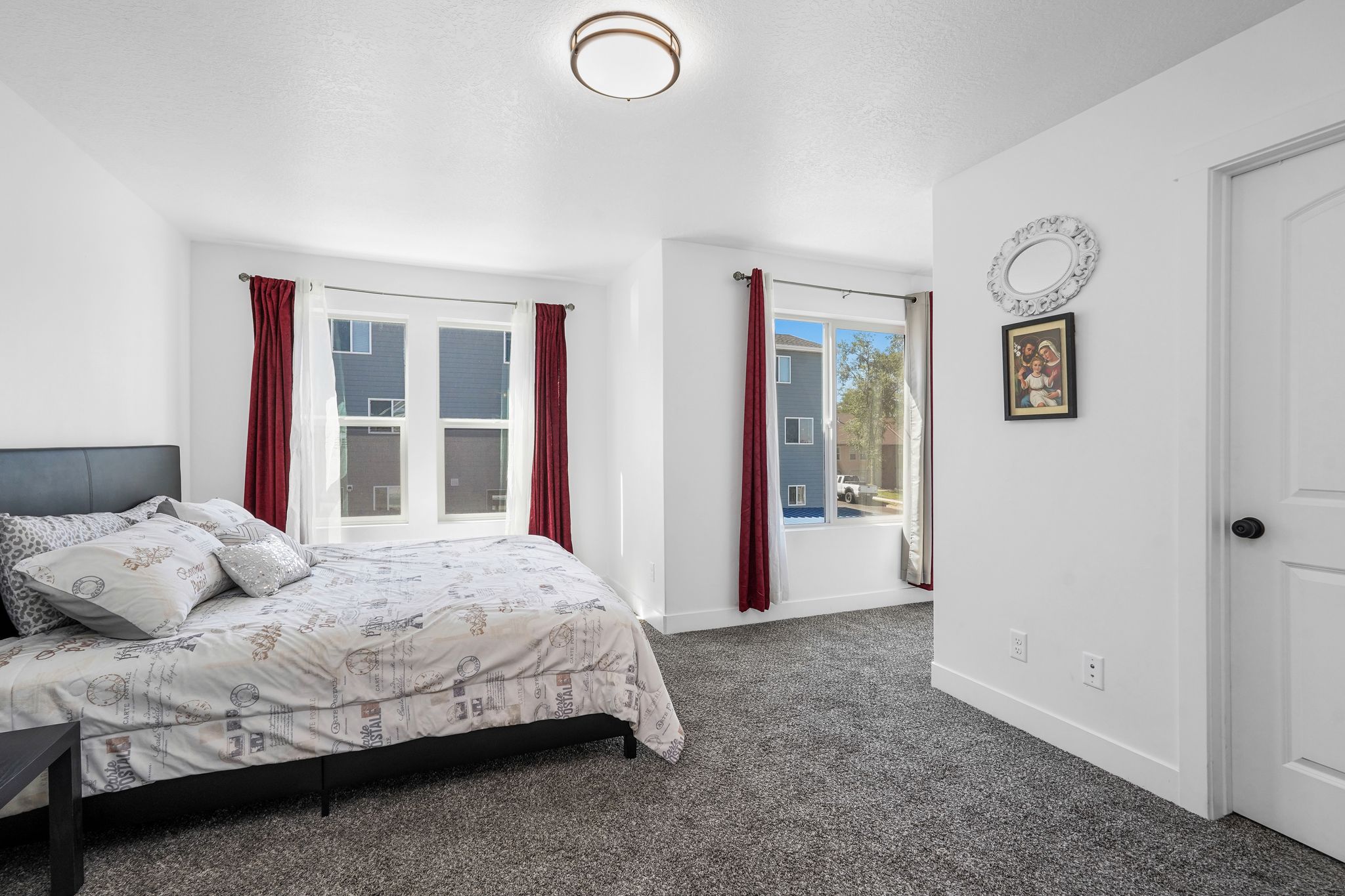 Carpeted bedroom featuring multiple windows with vertical blinds and drapes, a white paneled door, and a flush-mount ceiling light fixture