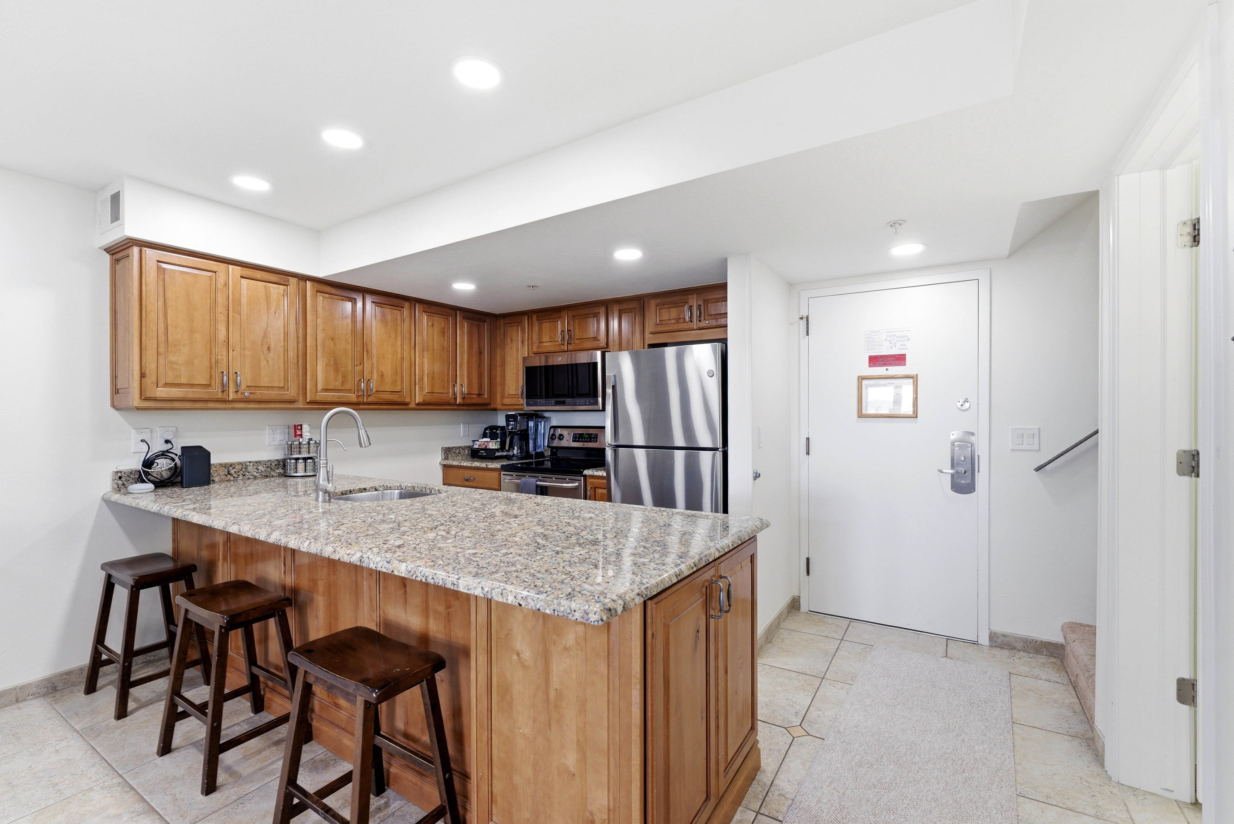 Kitchen with wood finish cabinetry, a peninsula, light stone counters, stainless steel appliances, and recessed lighting